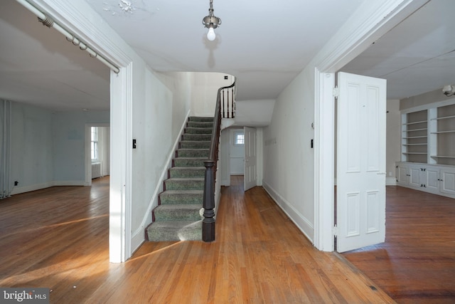 staircase with wood-type flooring and built in shelves