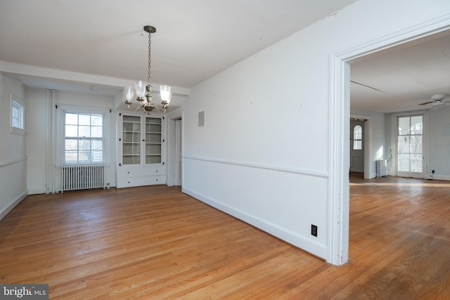 unfurnished dining area with radiator, ceiling fan with notable chandelier, and light hardwood / wood-style flooring