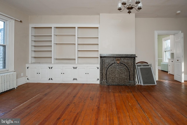 unfurnished living room featuring radiator heating unit, a notable chandelier, and dark hardwood / wood-style flooring