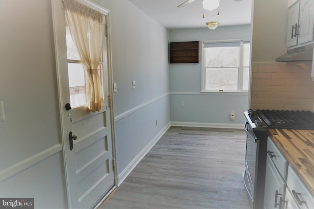 kitchen featuring decorative backsplash, gas range, ceiling fan, white cabinets, and butcher block countertops