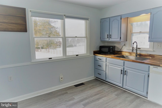 kitchen with butcher block countertops, plenty of natural light, white dishwasher, and sink