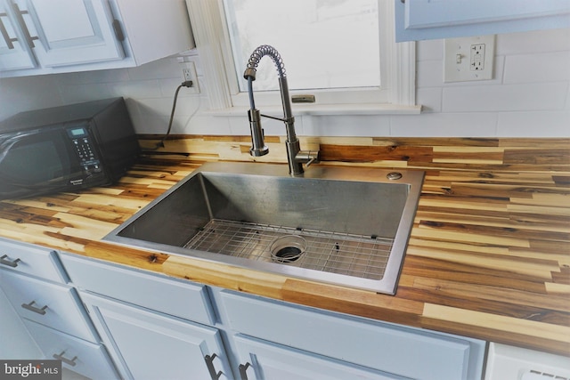 details featuring wood counters, white cabinets, tasteful backsplash, and sink