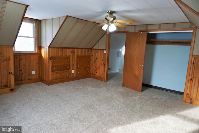 unfurnished bedroom with a closet, light colored carpet, ceiling fan, and wooden walls