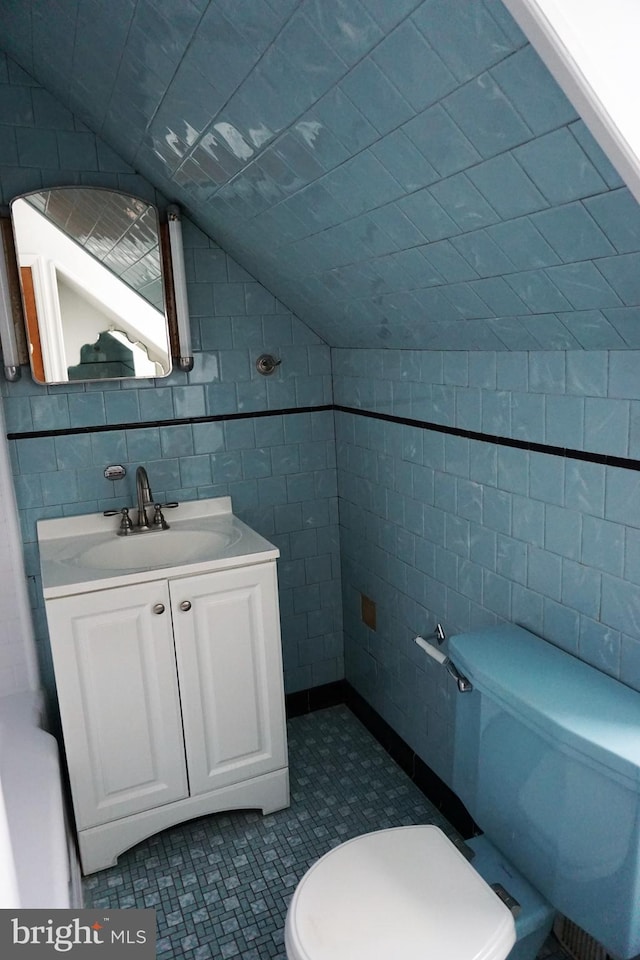 bathroom with vanity, toilet, tile walls, and lofted ceiling