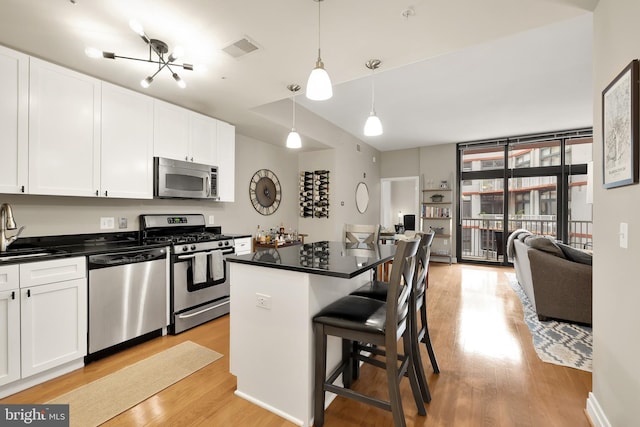 kitchen featuring white cabinets, decorative light fixtures, stainless steel appliances, and a breakfast bar area