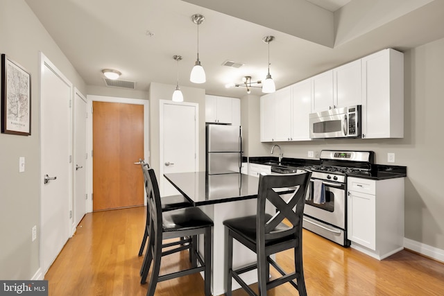 kitchen featuring white cabinetry, hanging light fixtures, stainless steel appliances, light hardwood / wood-style flooring, and a breakfast bar