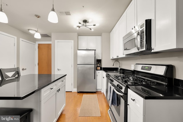 kitchen featuring pendant lighting, white cabinets, sink, light hardwood / wood-style flooring, and appliances with stainless steel finishes