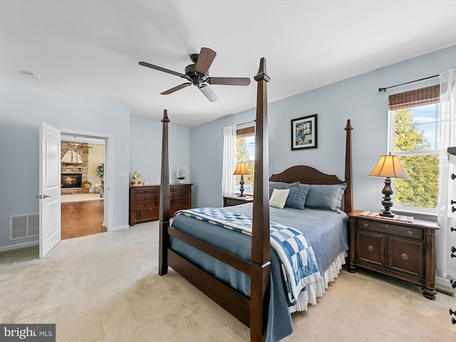 carpeted bedroom with a stone fireplace and ceiling fan