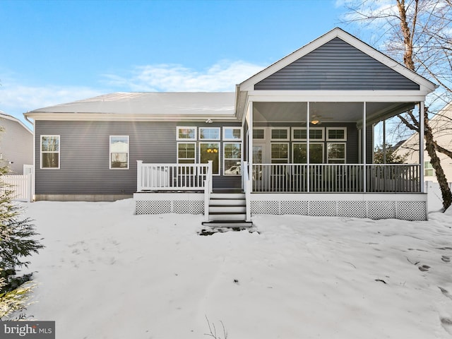 snow covered back of property with a sunroom and ceiling fan