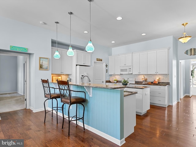 kitchen with white appliances, white cabinetry, hanging light fixtures, and an island with sink