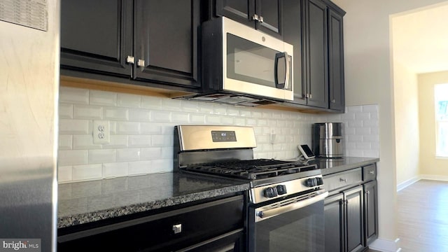 kitchen with appliances with stainless steel finishes, dark stone countertops, hardwood / wood-style floors, and tasteful backsplash