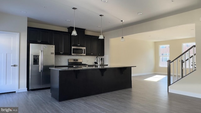 kitchen with decorative backsplash, stone countertops, a kitchen island with sink, appliances with stainless steel finishes, and a kitchen breakfast bar