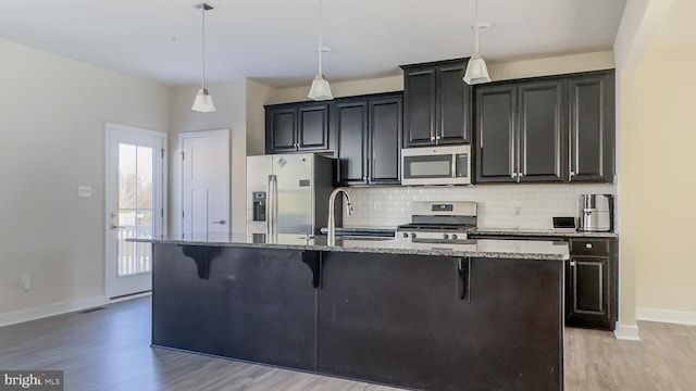 kitchen featuring appliances with stainless steel finishes, an island with sink, a breakfast bar, sink, and decorative light fixtures