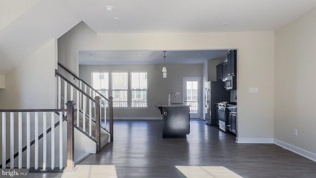 interior space featuring dark hardwood / wood-style floors, hanging light fixtures, an island with sink, stainless steel appliances, and stone counters