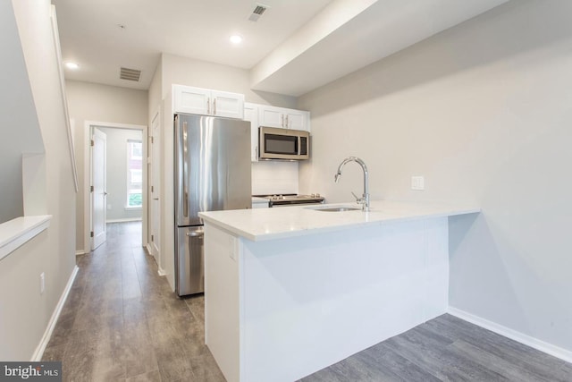 kitchen featuring white cabinets, sink, hardwood / wood-style flooring, appliances with stainless steel finishes, and kitchen peninsula