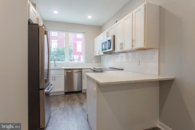 kitchen with dark wood-type flooring, white cabinets, light stone countertops, kitchen peninsula, and stainless steel appliances