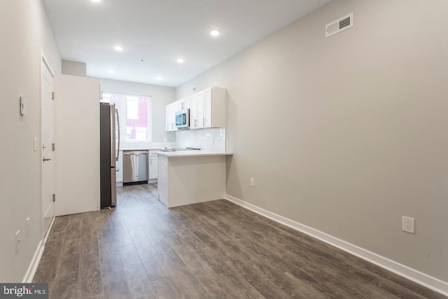 kitchen with stainless steel appliances, dark hardwood / wood-style floors, kitchen peninsula, decorative backsplash, and white cabinets