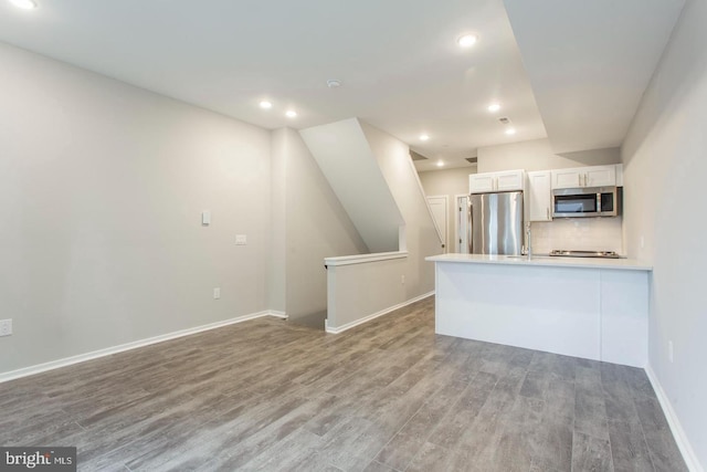 kitchen with white cabinets, kitchen peninsula, appliances with stainless steel finishes, tasteful backsplash, and wood-type flooring