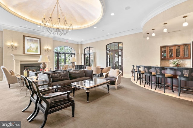 carpeted living room featuring french doors, a raised ceiling, a notable chandelier, bar area, and ornamental molding