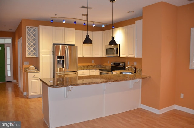 kitchen featuring kitchen peninsula, stainless steel appliances, white cabinets, and dark stone counters