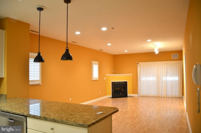 kitchen with white cabinetry, hanging light fixtures, stainless steel dishwasher, dark stone counters, and light hardwood / wood-style floors