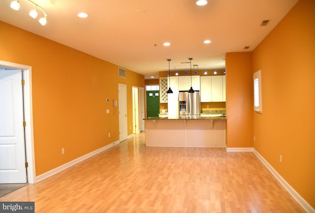 kitchen with kitchen peninsula, stainless steel refrigerator with ice dispenser, light hardwood / wood-style floors, and pendant lighting