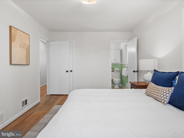 bedroom featuring visible vents, baseboards, ensuite bath, and wood finished floors