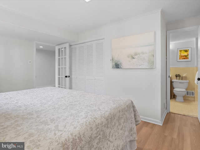 bedroom with visible vents, wood finished floors, a closet, tile walls, and crown molding