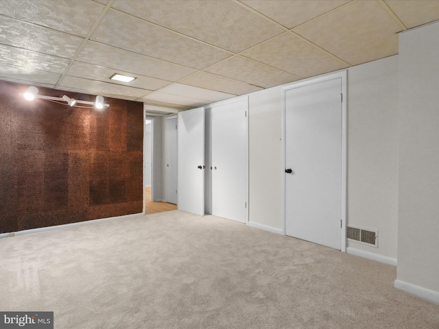 finished basement featuring visible vents, a paneled ceiling, carpet, and baseboards