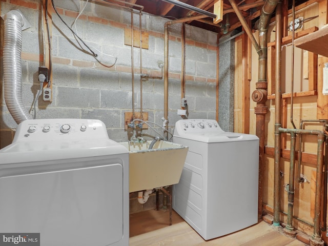 clothes washing area featuring laundry area, independent washer and dryer, wood finished floors, and a sink