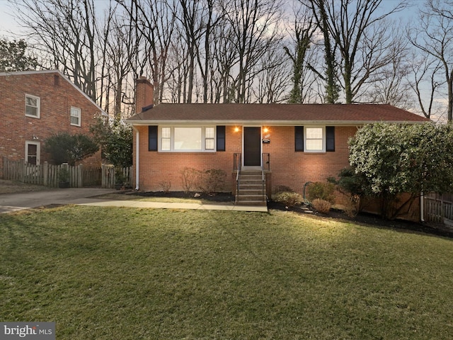 view of front of house with brick siding, a chimney, a front lawn, and fence