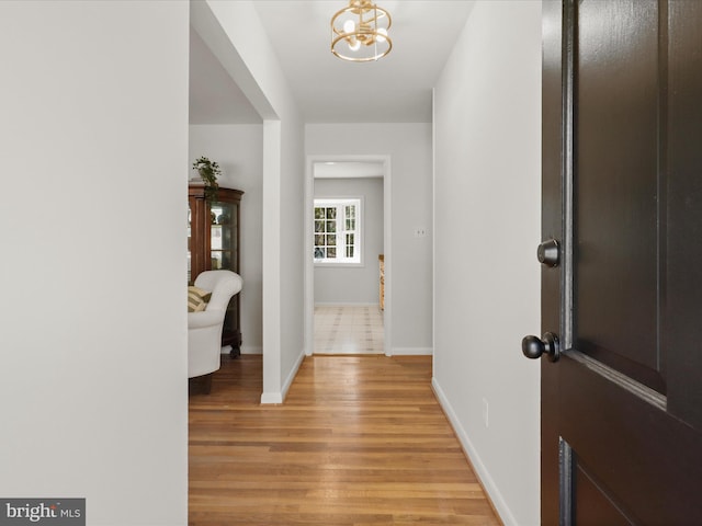 corridor featuring an inviting chandelier, light wood-style flooring, and baseboards