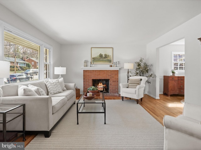 living room with plenty of natural light, a brick fireplace, baseboards, and wood finished floors