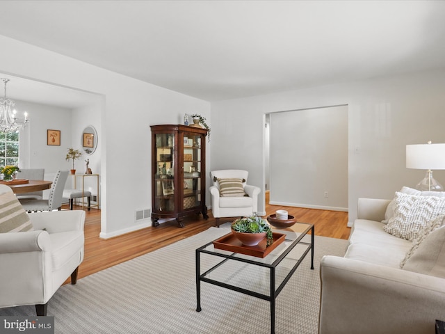 living area with a chandelier, visible vents, baseboards, and wood finished floors