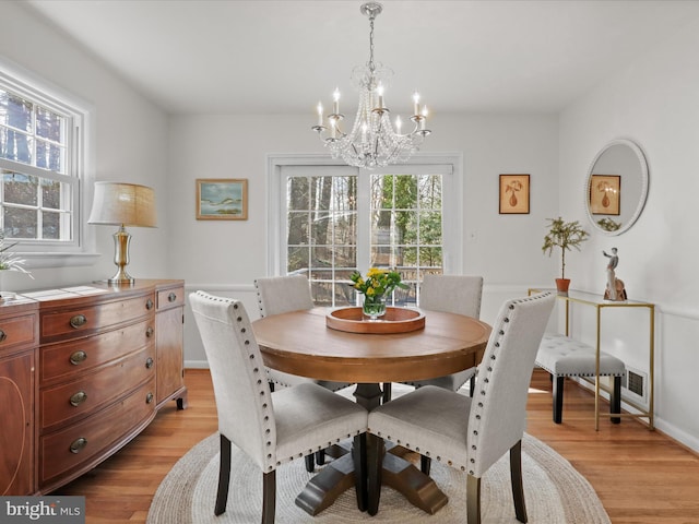 dining space with baseboards, a chandelier, and light wood finished floors