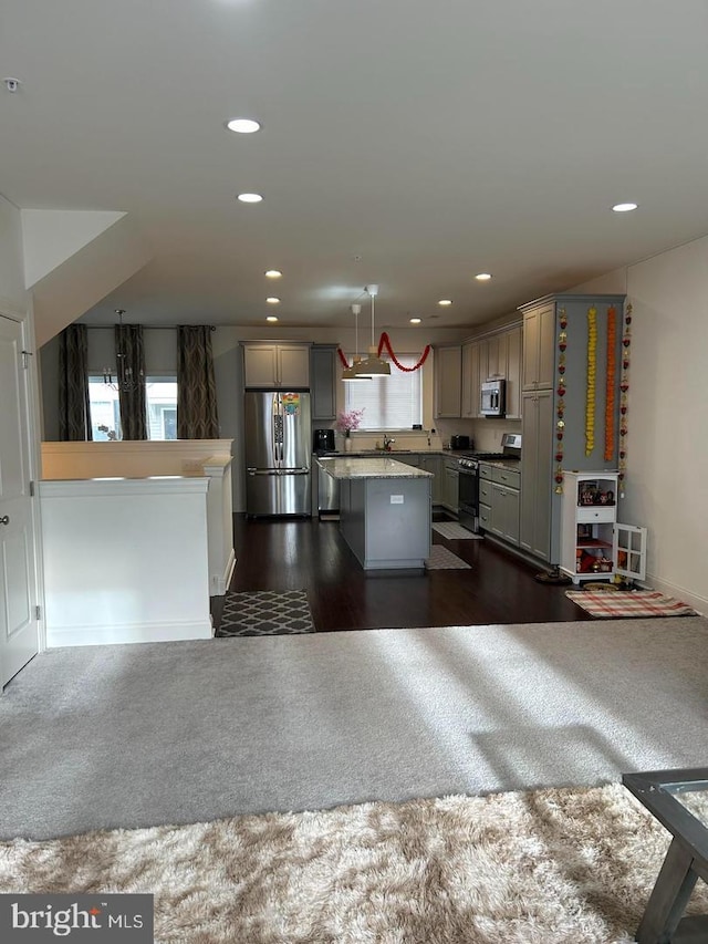 kitchen with dark carpet, hanging light fixtures, gray cabinets, appliances with stainless steel finishes, and a kitchen island