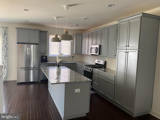 kitchen featuring gray cabinetry, a center island, hanging light fixtures, appliances with stainless steel finishes, and light stone counters