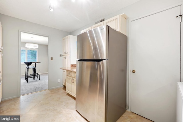 kitchen with light stone counters, stainless steel fridge, light colored carpet, decorative light fixtures, and cream cabinetry