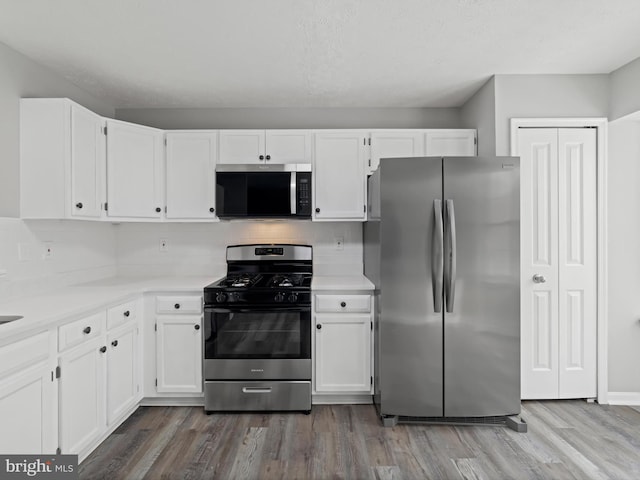 kitchen featuring wood-type flooring, stainless steel appliances, white cabinetry, and tasteful backsplash