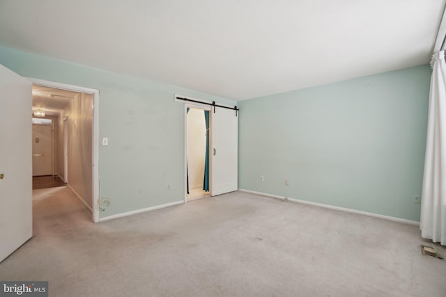 unfurnished bedroom with a barn door and light colored carpet