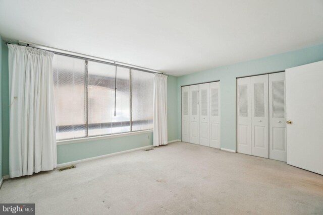 unfurnished bedroom featuring light carpet and multiple closets