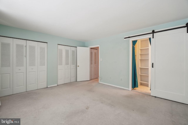 unfurnished bedroom with two closets, a barn door, light colored carpet, and ensuite bath