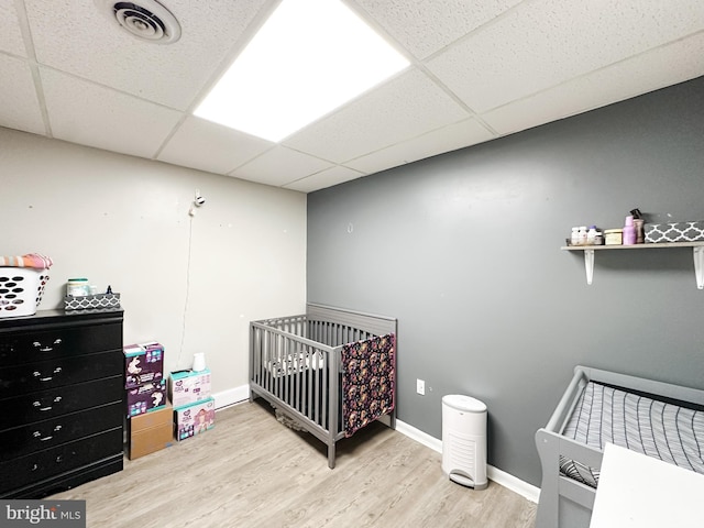 bedroom with a paneled ceiling, a crib, and hardwood / wood-style flooring