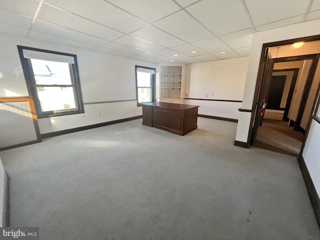 spare room with built in shelves, a drop ceiling, and light colored carpet