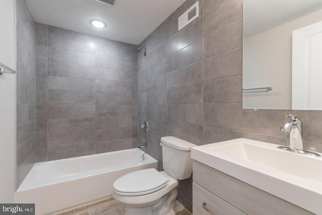 full bathroom with vanity, tiled shower / bath combo, tile walls, and toilet