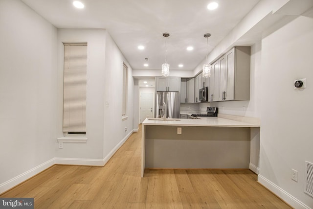 kitchen featuring kitchen peninsula, appliances with stainless steel finishes, light wood-type flooring, gray cabinetry, and pendant lighting