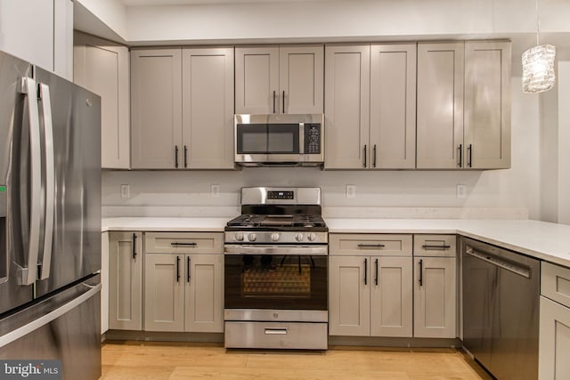 kitchen with gray cabinets, hanging light fixtures, stainless steel appliances, and light hardwood / wood-style floors