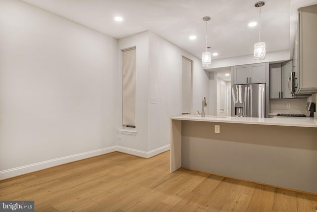 kitchen with kitchen peninsula, gray cabinetry, sink, decorative light fixtures, and stainless steel fridge with ice dispenser