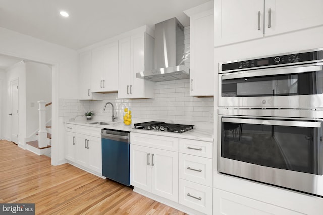 kitchen featuring wall chimney range hood, tasteful backsplash, light hardwood / wood-style flooring, white cabinets, and appliances with stainless steel finishes