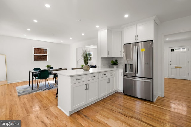 kitchen with stainless steel refrigerator with ice dispenser, light wood-type flooring, tasteful backsplash, white cabinetry, and kitchen peninsula